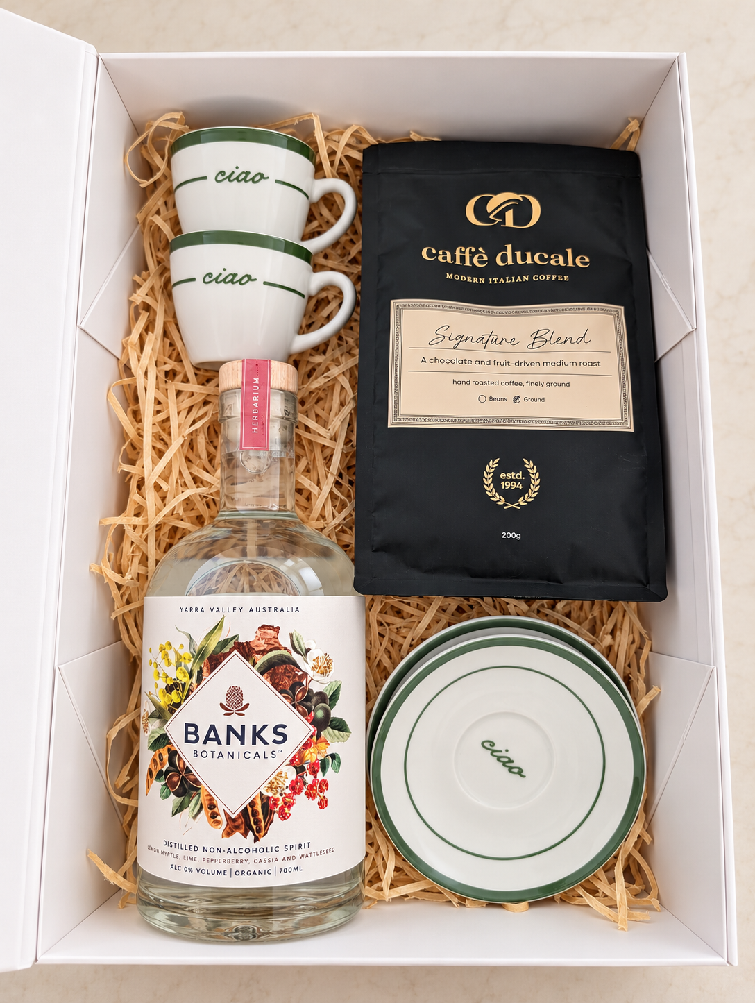 Botanical Café non-alcoholic gift box with Banks Botanicals Herbarium, Caffè Ducale coffee, two green-trimmed espresso cups and matching saucers.