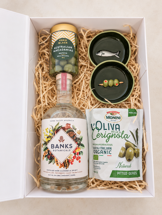 The Botanical Pause non-alcoholic gift box with Banks Botanicals Herbarium, olives, matcha macadamias and two green ceramic dishes.